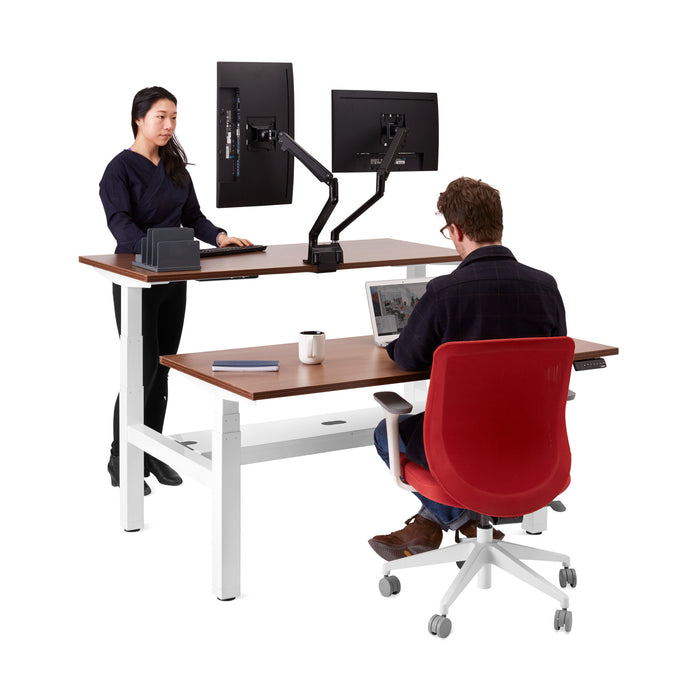 Two professionals working at an ergonomic office setup with adjustable desks and dual monitor arms. (Walnut-57&quot;)