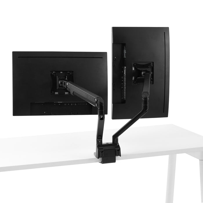 Dual monitors mounted on adjustable arms attached to a white desk against a white background. (Black)