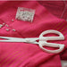 Close-up of sewing scissors on a vibrant pink fabric with pearls and pin box. (White)