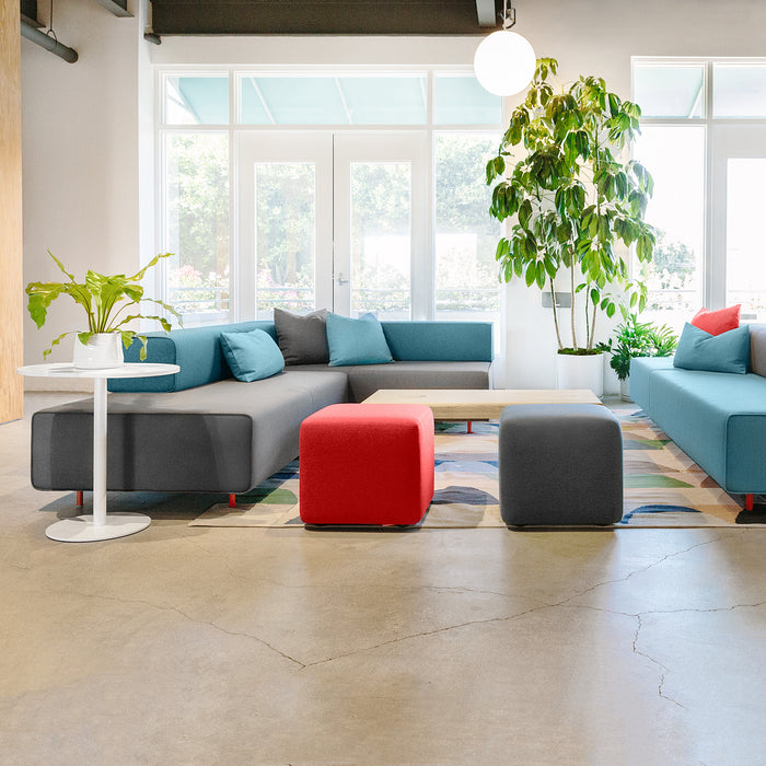 Modern office lounge area with blue sofa, red ottoman, and indoor plants. (Dark Gray)