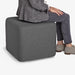 Woman seated on a gray modern ottoman with casual attire. (Dark Gray)