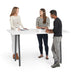 Three colleagues conversing at a white standing table in a bright office setting. (White-72&quot; x 36&quot;)(White-72&quot; x 36&quot;)