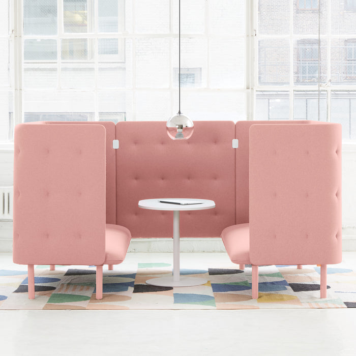 Modern pink private booth seating in a bright office space with a white table and colorful rug. 
