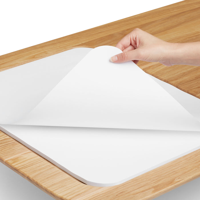 Person peeling adhesive liner from the corner of a product on a wooden surface. 