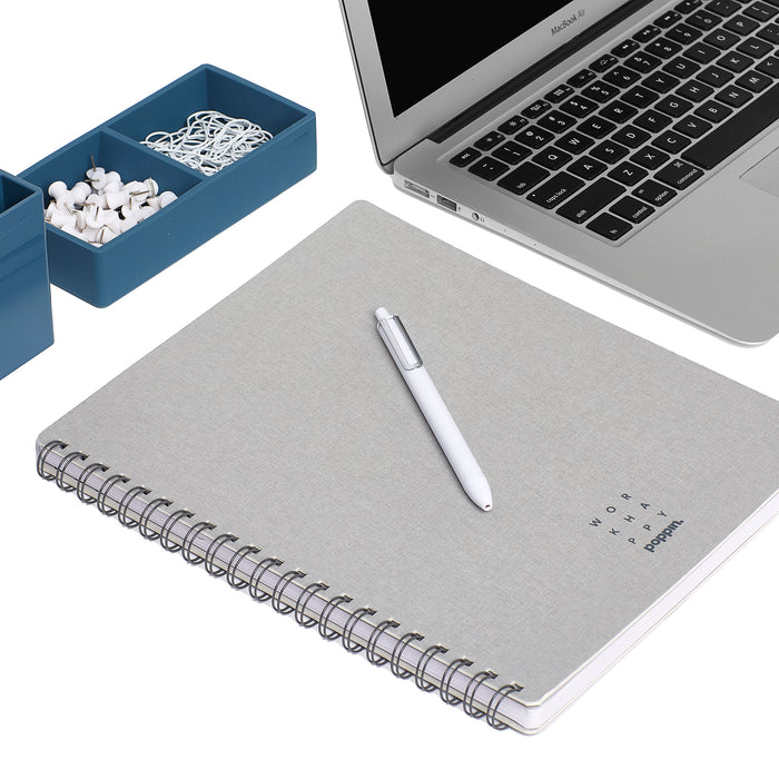 Grey spiral notebook with pen on desk next to laptop and stationery holder. (Light Gray)