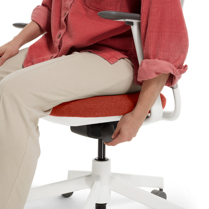 Person adjusting the height of a red ergonomic office chair (Dorset Cayenne-White)