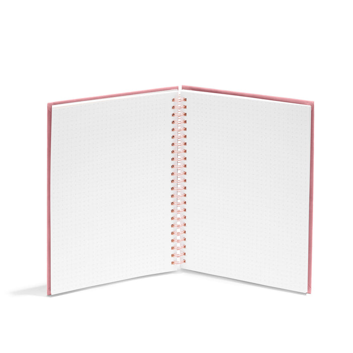 Open spiral notebook with dotted pages and pink cover on white background. (Dusty Rose)
