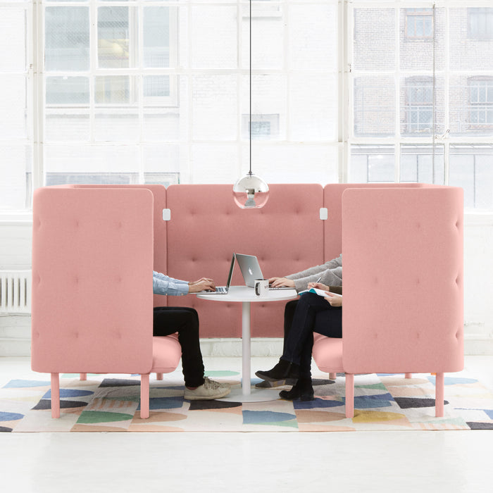 Two people seated facing away in pink privacy work pods with a laptop on the table between them. (Blush-Blush)