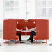 "Two professionals working on laptops in modern office privacy booths with red dividers." (Brick-Brick)