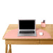 Laptop on wooden desk with pink mat, white mouse, and pink pen holder against white background. (Blush)