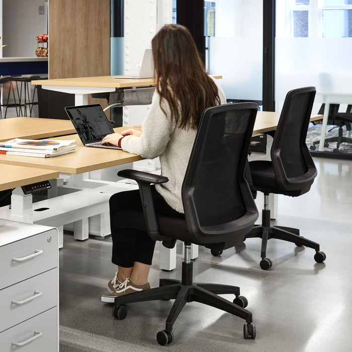Woman working on laptop in modern office space with ergonomic chairs. (Black)
