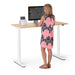 Woman in a patterned dress standing at an adjustable standing desk with a computer monitor (Natural Oak-47&quot;)