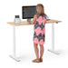 Woman standing at a modern height-adjustable desk with computer and accessories. (Natural Oak-57&quot;)