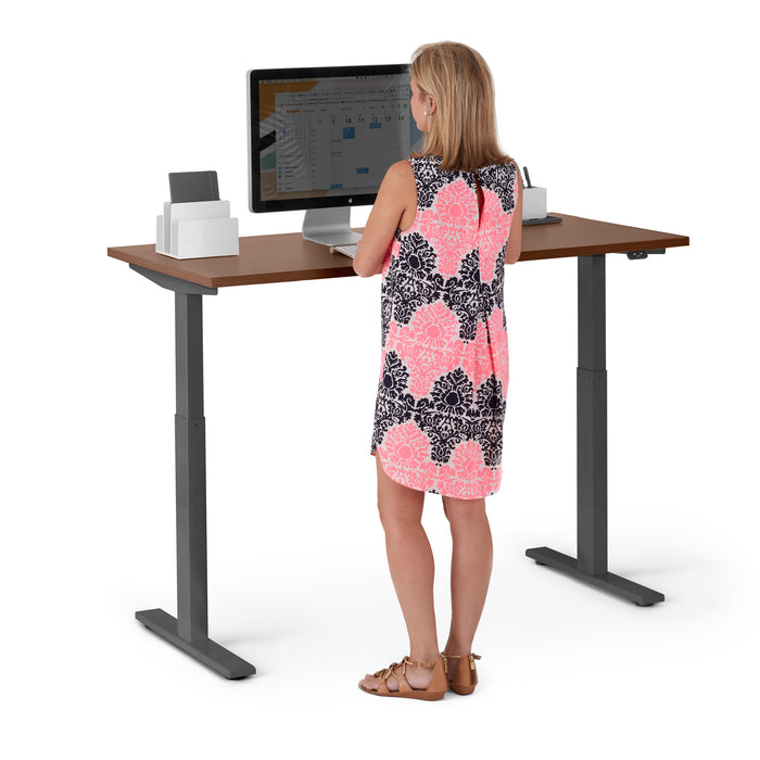 Woman standing at adjustable standing desk with computer and accessories. (Walnut-47&quot;)