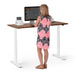 Woman standing at an adjustable desk working on a computer. (Walnut-57&quot;)