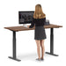 Woman standing at a modern height-adjustable desk working on a desktop computer. (Walnut-60&quot;)
