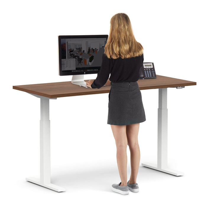 Woman standing at an adjustable desk using a computer in an office setting. (Walnut-60&quot;)