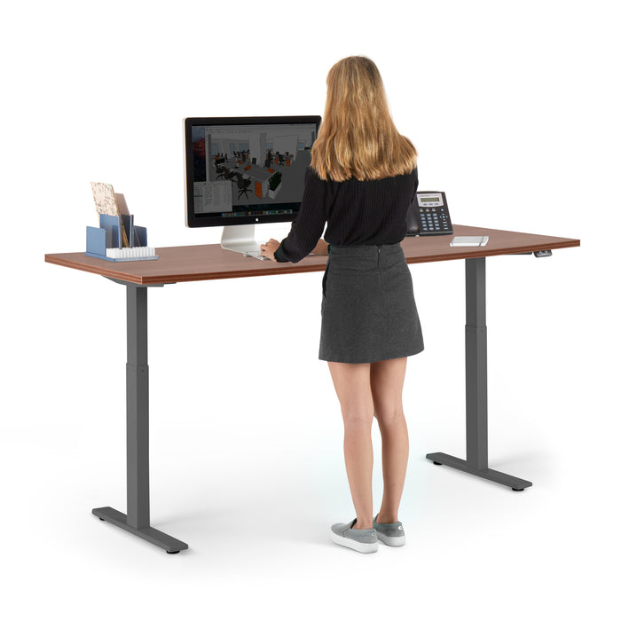 Woman standing at modern adjustable standing desk with computer and office supplies. (Walnut-72&quot;)