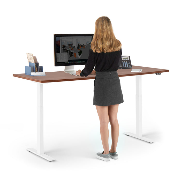 Woman standing at a modern adjustable standing desk working on a computer (Walnut-72&quot;)
