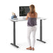 Woman standing at a modern height-adjustable desk with computer and notebook. (White-47&quot;)