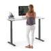 Woman standing at a modern adjustable standing desk with computer and office supplies. (White-57&quot;)