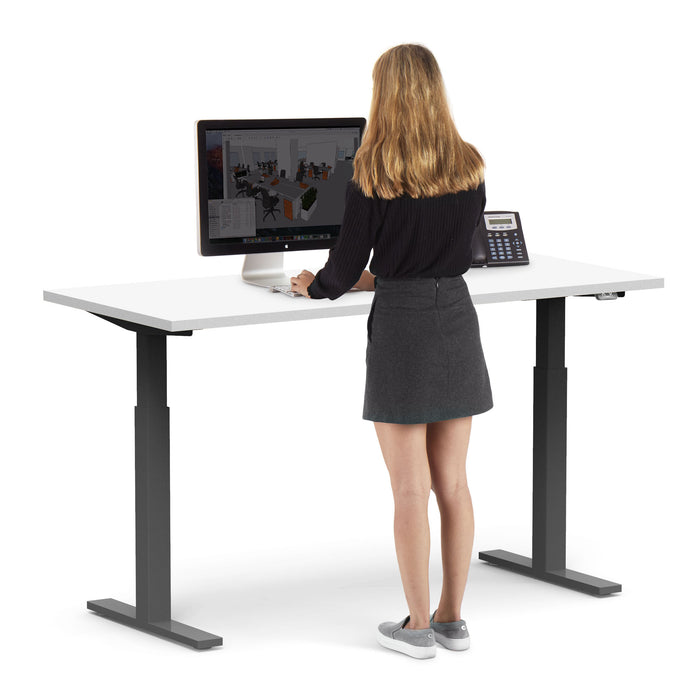Woman standing and working at a modern height-adjustable desk with a computer. (White-60&quot;)