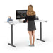 Woman standing at a modern height-adjustable desk working on a computer in a bright office setting. (White-72&quot;)