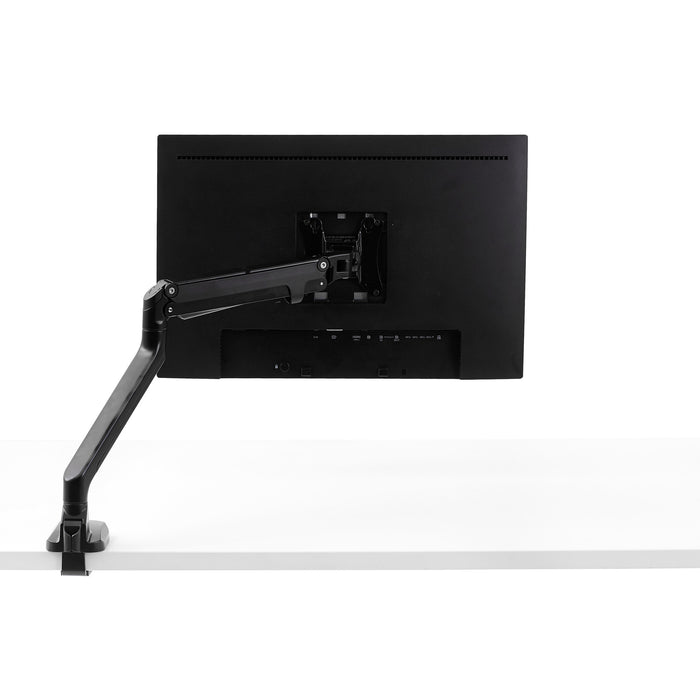 Articulated monitor arm attached to a desktop holding a flat screen monitor in a white studio setup. (Black)