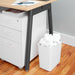 White trash bin filled with crumpled paper under office desk with filing cabinet. (White)