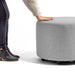 Person in jeans and boots touching a gray fabric ottoman on a white background. (Gray)