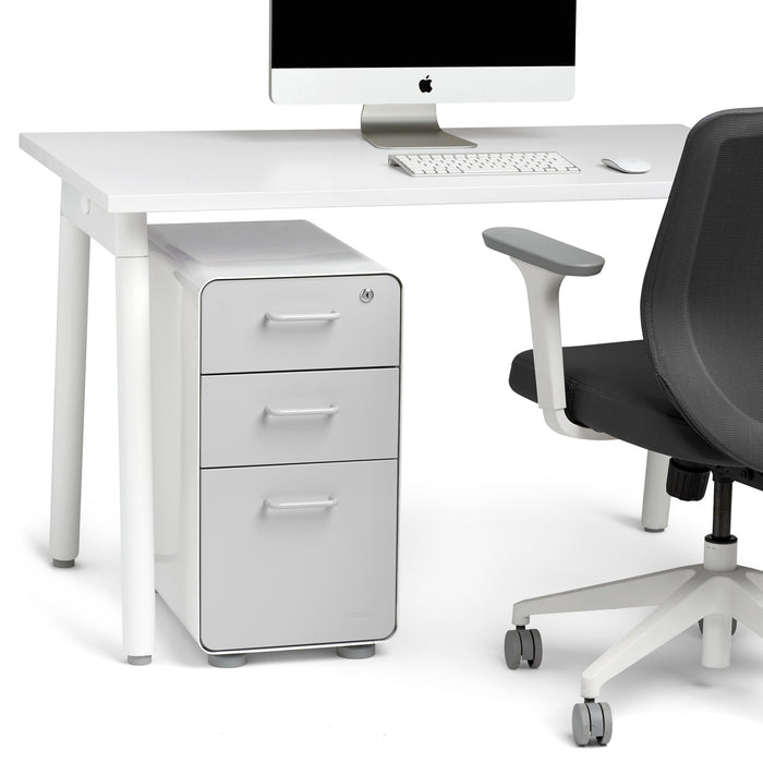 Modern white office desk with Apple computer, white file cabinet, and ergonomic black chair. (Light Gray-White)