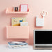 Home office corner with laptop and organized wall shelves against a pink background. (White)
