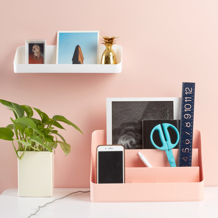 Modern home office desk organization with plants, smartphone, and decor against a pink wall. (White)