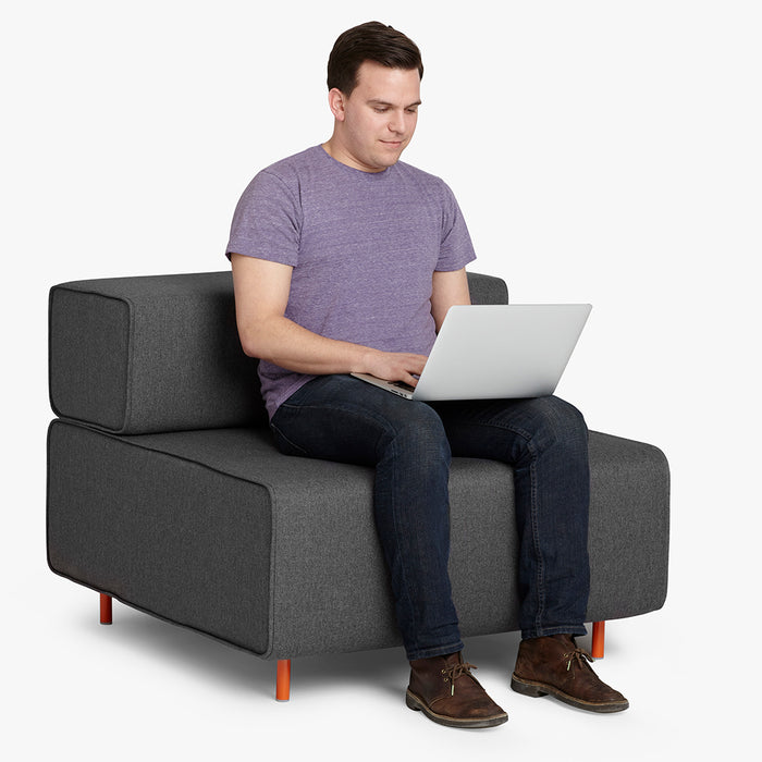 Man in casual clothes working on laptop while sitting on a modern gray sofa. (Dark Gray-Dark Gray)