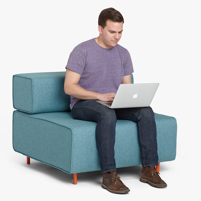 Man sitting on blue sofa working on laptop with a white background. (Dark Blue-Dark Blue)(Dark Gray-Dark Blue)