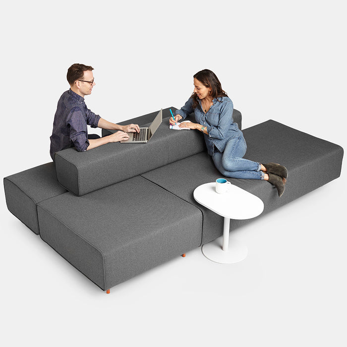 Two people collaborating on laptops on a modular sofa with a round side table. (Dark Gray-Dark Gray)