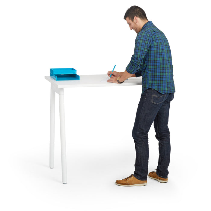 Man standing and writing on paper at a white modern desk with blue organizers 