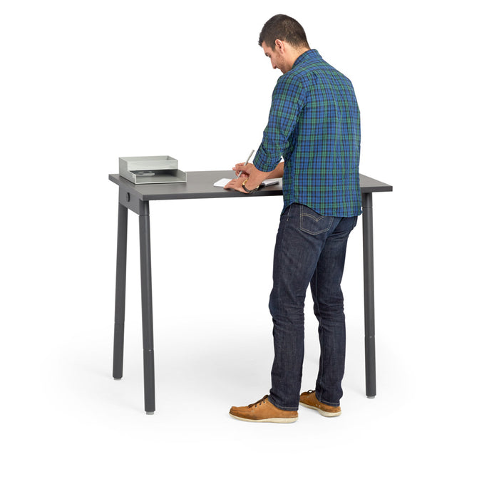 Man in casual attire standing and writing at a modern grey desk with a book on 