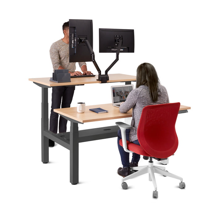 Man standing and woman sitting at a modern height-adjustable desk with dual computer monitors. (Natural Oak-47&quot;)