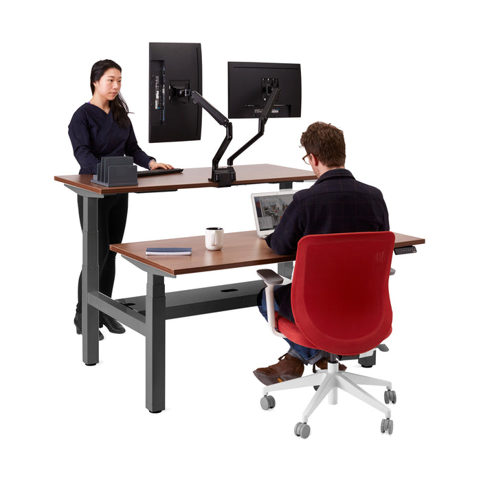 Two professionals working at an ergonomic standing desk with monitors in an office setting. (Walnut-57&quot;)